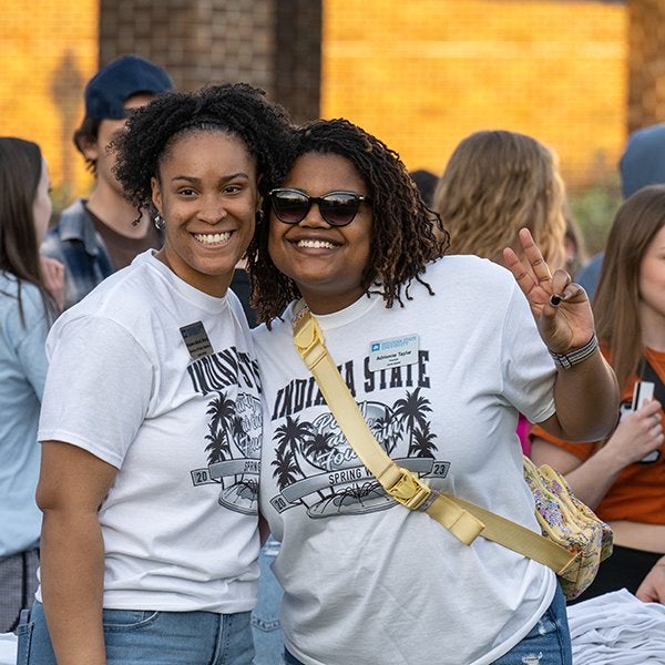 Two students wearing black and white Spring Week t-shirts smile for the camera.