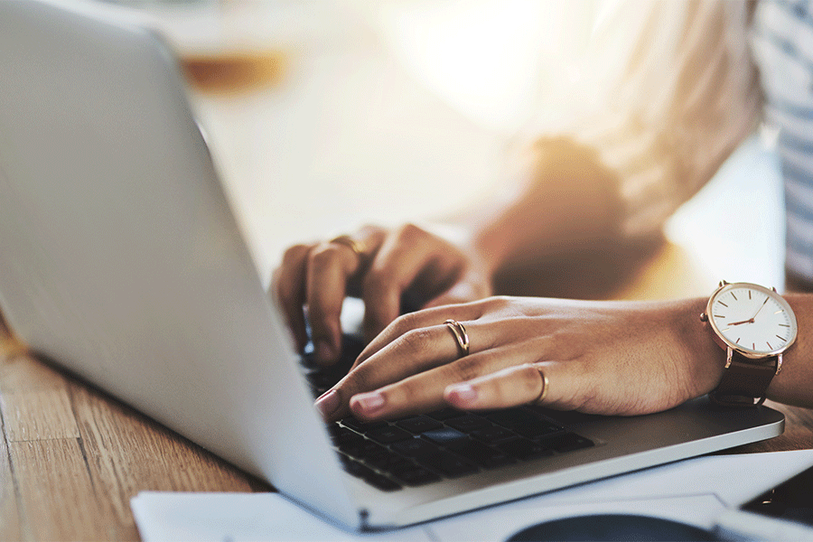 Detailed image of the hands of a Black female typing on a laptop computer. 