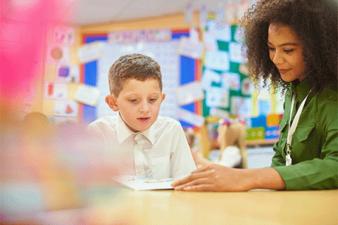 A primary aged schoolboy sits with his teacher in a one-on-one reading session. 